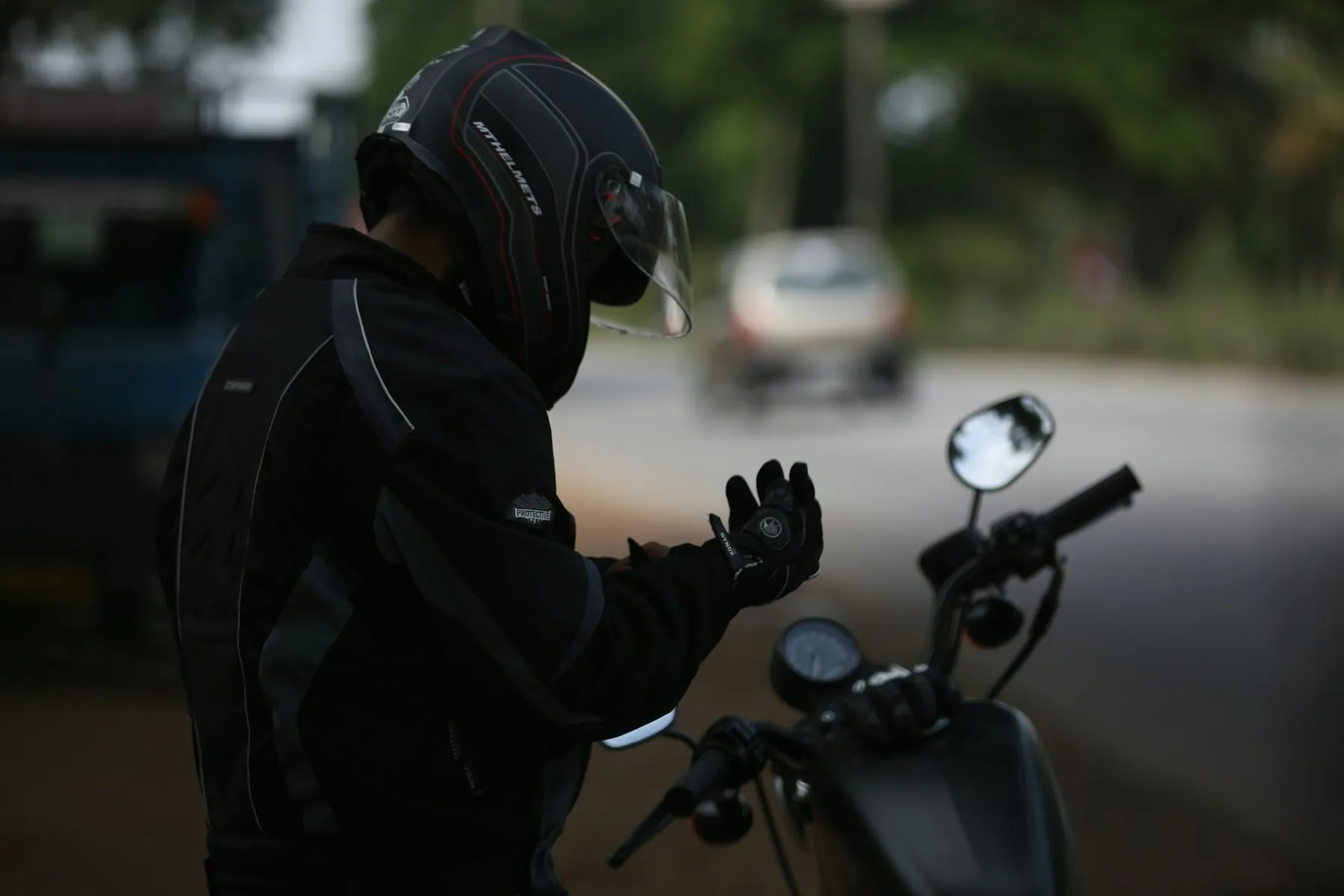 A rider in a black riding suit and helmet at the handlebars of a scooter on a city street