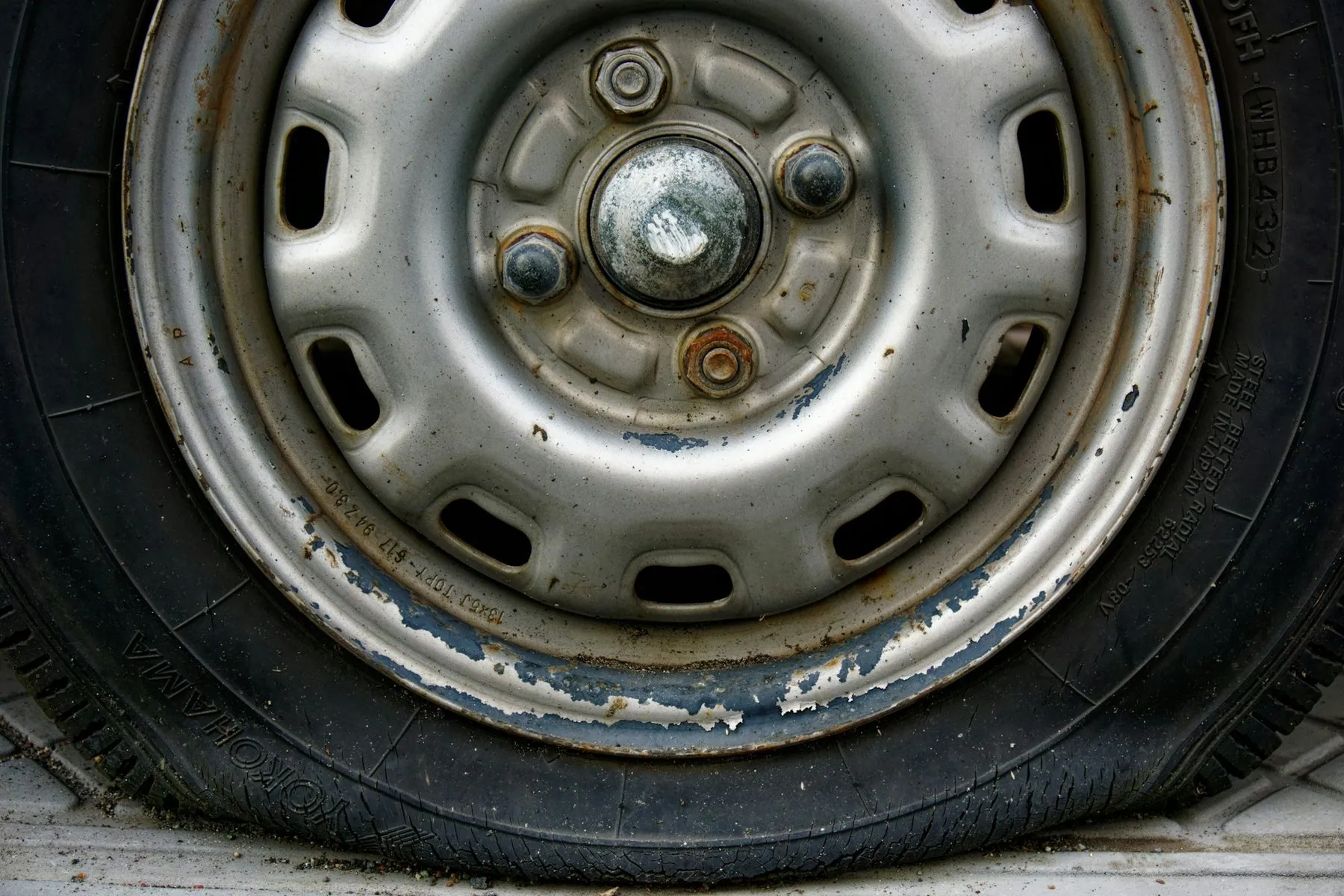 A close-up of a bare steel wheel with a flat, badly worn tyre sagging onto the rim