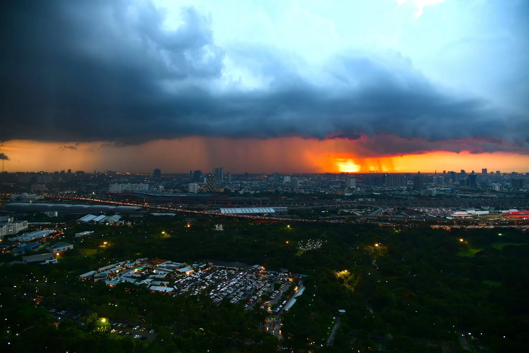 A wall of monsoon rain moving across the Bangkok skyline under a black storm cloud at sunset