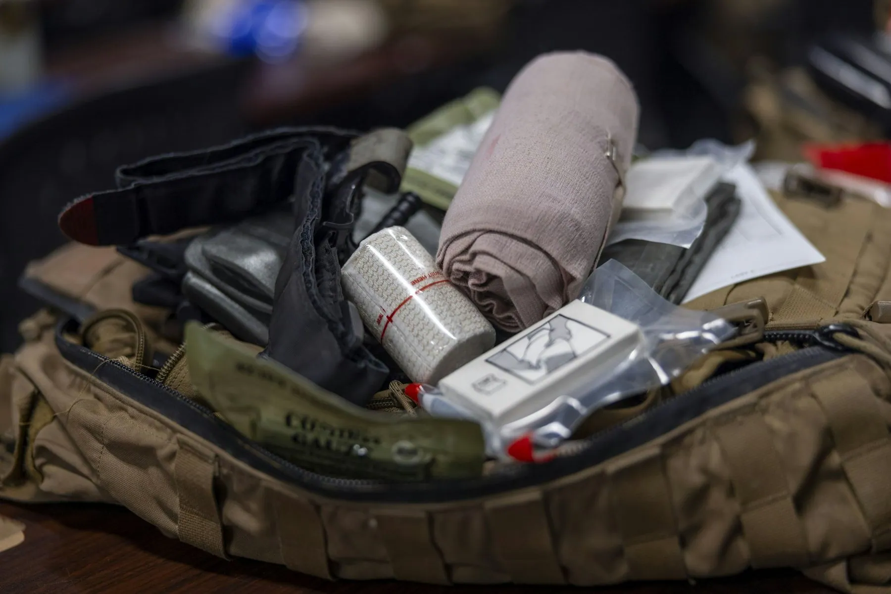 An opened first-aid pouch with rolled bandages, dressings and tape laid out inside it