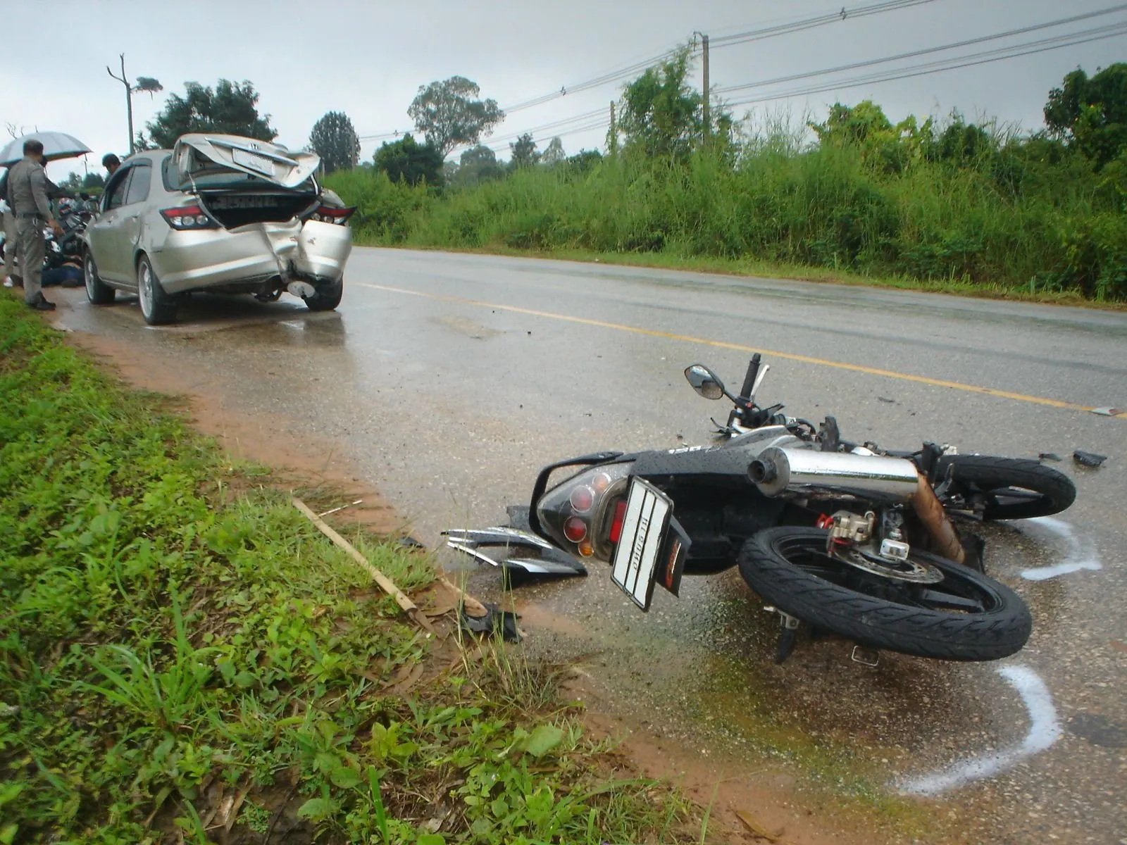 A motorbike lying on its side on a wet rural road with the car it hit stopped a few metres beyond it
