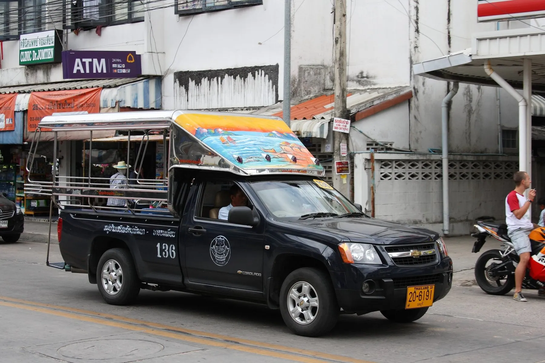 A black pickup converted into a songthaew, benches under a canopy in the bed, pulling along a Pattaya street
