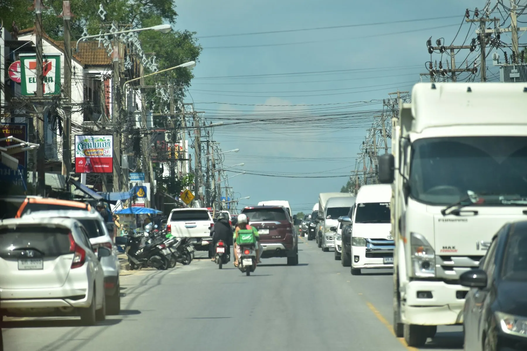 A busy Koh Samui street with lorries, pickups and scooters sharing the lane in both directions