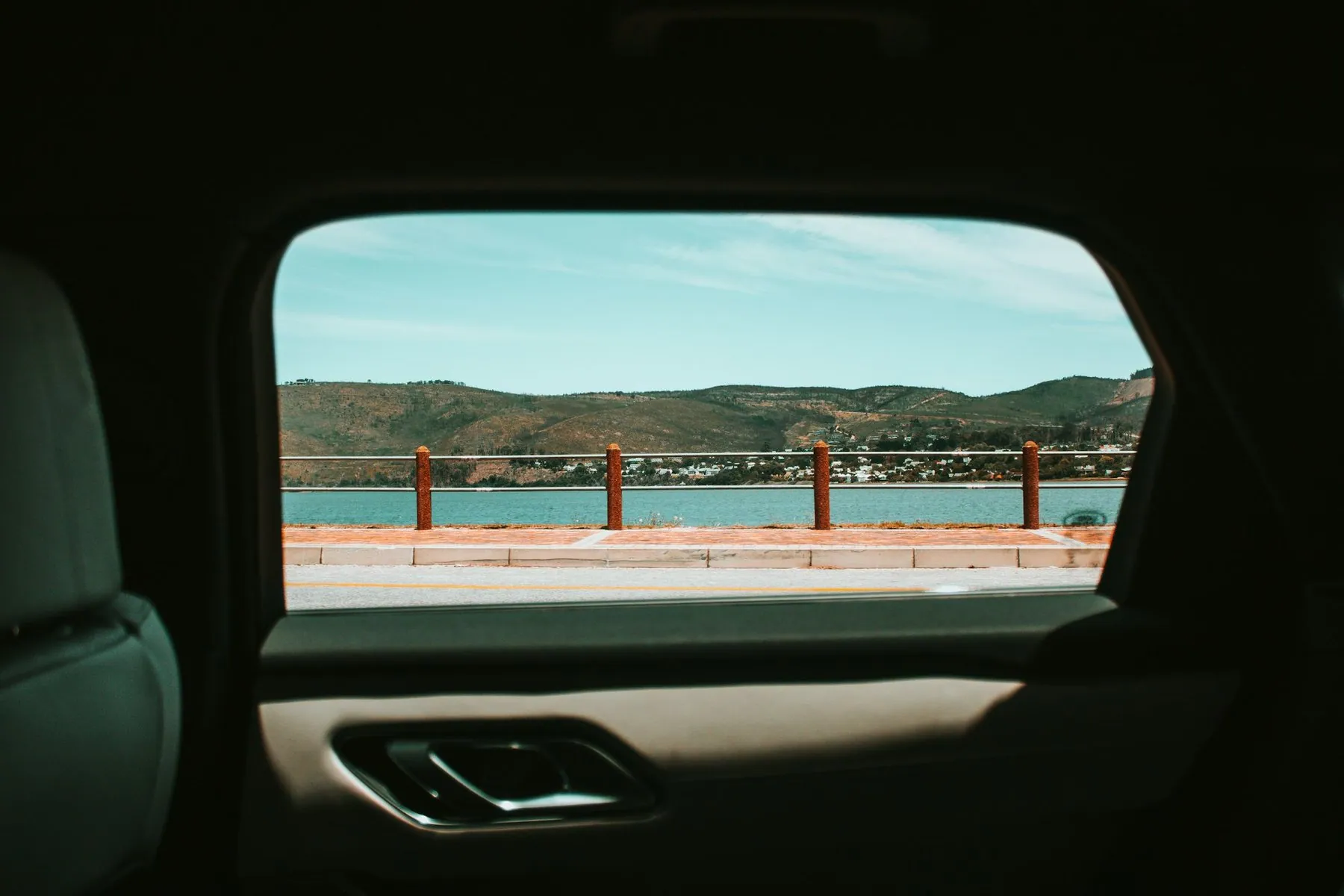The view out of a vehicle's rear side window, the interior in deep shadow against the bright landscape outside