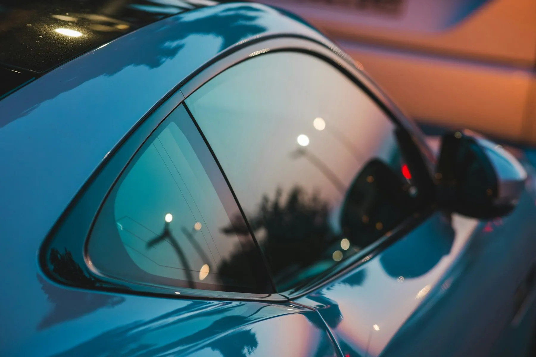 A close-up of a car's dark tinted side window and door mirror, the street behind it reduced to a blur