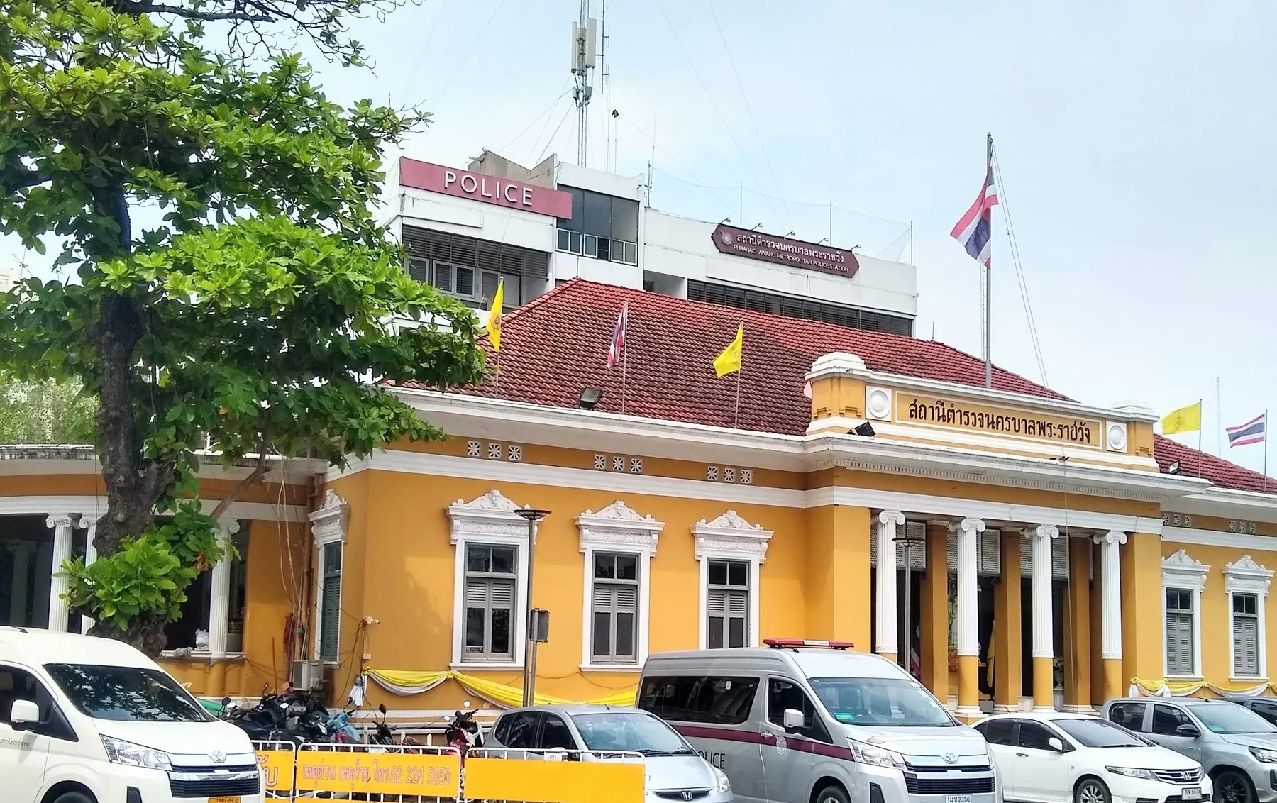 The yellow colonial-era frontage of Phra Ratchawang police station in Bangkok, cars parked along the kerb outside