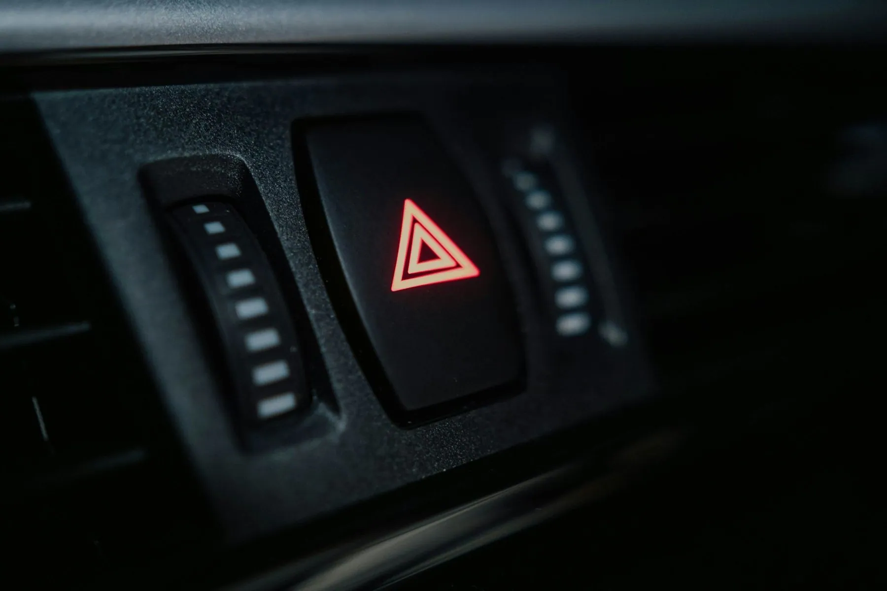 A car's hazard-warning switch on the dashboard, the red triangle lit