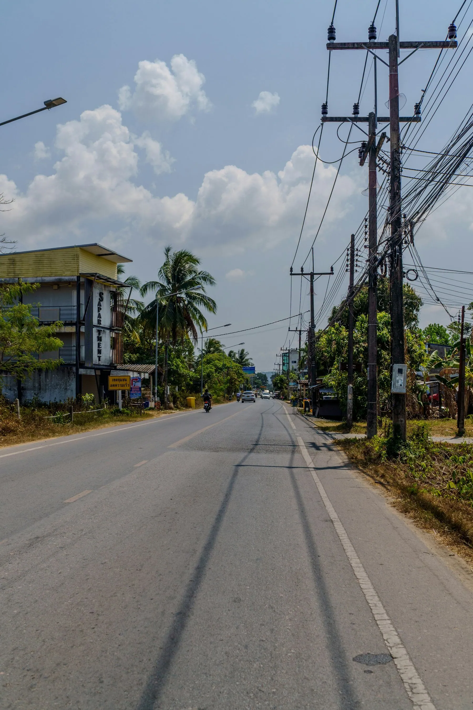 A straight empty road in Thailand running away between concrete power poles and low roadside buildings